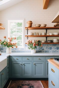 a kitchen with blue cabinets and white counter tops, flowers in vases on the window sill