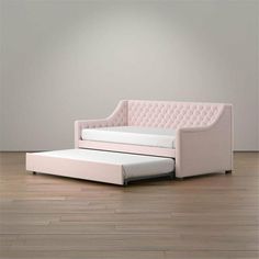 a pink couch with a pull out bed in front of a gray wall and wooden floor