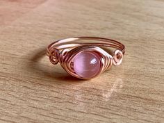 Who doesn't love rose gold? I know I'm in love with it because it's so beautiful and makes unique jewelry looks. This fun ring has a 6mm pink cat's eye wrapped in 20 gauge rose gold colored wire. The wire is silver plated with a tarnish resistant coating to prevent wear and color change. This ring is simple and dainty with a swirl design on either side of the stone. Cat's eye is a beautiful, man made stone with a brilliant flash that dances in the light. Check out the cat's eye section of my sho Adjustable Rose Quartz Rose Gold Ring, Wire Wrapped Rose Gold Rings, Cat Eye Bracelet, Cats Eye Ring, Mermaid Glass, Selling Handmade Items, Wire Wrapped Ring, Diffuser Jewelry, Wire Wrapped Bracelet