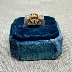 a gold and silver ring sitting on top of a blue velvet box with a diamond in the middle