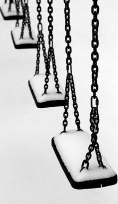 black and white photograph of snow covered swings in the wintertime with chains hanging from them