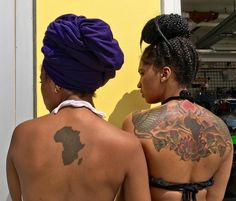 two women with tattoos on their back standing next to each other in front of a yellow wall