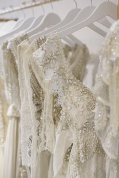 wedding dresses hanging on a rack in a bridal room, with beading and sequins