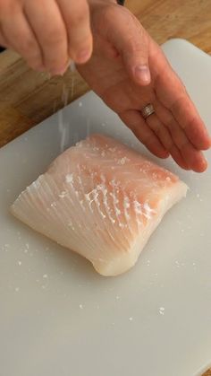 a person is sprinkling salt onto a fish on a cutting board with a knife