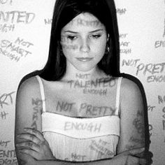 a woman standing in front of a wall with writing all over her chest and arms crossed