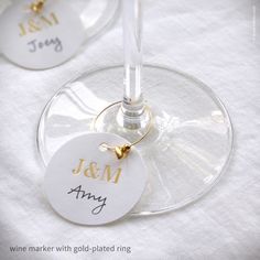 two wine glasses sitting on top of a white table cloth with gold lettering and charms