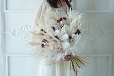 a woman in a white dress holding a bouquet of flowers with feathers on her arm