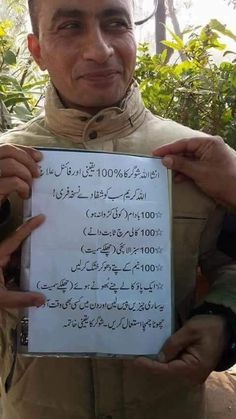 a man holding up a paper with writing on it in front of some trees and bushes