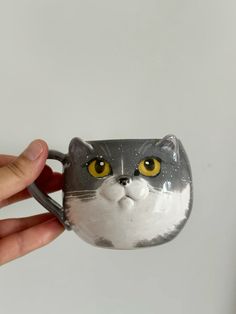 a hand holding a ceramic cat mug with yellow eyes