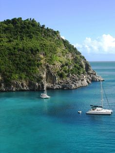 two boats floating in the blue water next to a rocky cliff and green trees on top of it