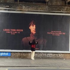 a man standing in front of a large poster on the side of a building next to a street