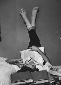 two people laying in bed with their feet up on each other's head and reading books