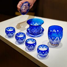 blue glass dishes and cups sitting on a white counter top with one hand reaching for the bowl