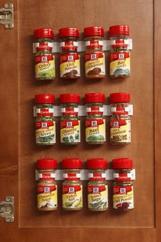 several jars of spices are hanging on the wall in front of a wooden cabinet door