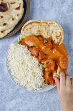 a person is holding a piece of bread over rice with chicken and sauce on it