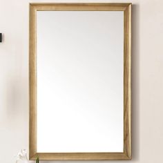 a bathroom mirror sitting on top of a wooden shelf next to a white vase filled with flowers