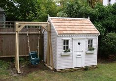 a small white shed with a swing set next to it and a green bucket in the yard