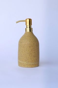 a yellow soap dispenser on a white surface with a gold faucet