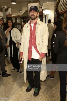 a man in a red shirt and white trench coat standing in front of a group of people