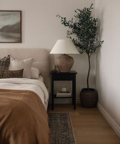 a bedroom with a bed, nightstand and plant on the side table in front of it