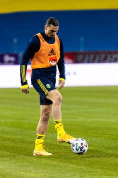 a soccer player is kicking a ball on the field with yellow socks and an orange shirt