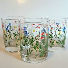 four glasses with flowers painted on them sitting on a table