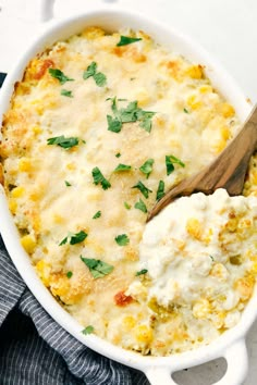 a casserole dish with cheese and parsley on top, next to a wooden spoon