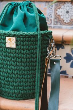 a green crocheted bag sitting on top of a wooden table next to a keychain