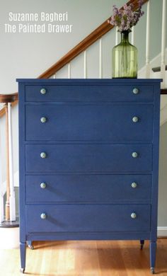 a blue dresser with flowers in a vase on top and the words suzanne bagheri painted drawer above it