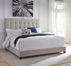 a white bed sitting in a bedroom on top of a hard wood floor next to a window