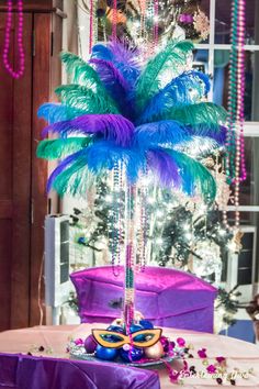 a table topped with a purple and blue centerpiece next to a tree covered in beads