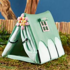 a green toy house with a flower on the front and side door is sitting in grass