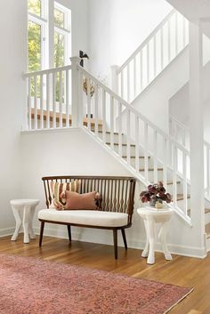 a living room with a white staircase and wooden bench next to a rug on the floor