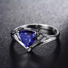 a ring with a blue triangle shaped stone and two white diamonds on the side, sitting on