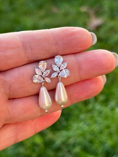 a hand holding a pair of earrings in it's left hand with grass behind it