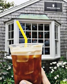 a person holding up a drink in front of a building with a yellow straw sticking out of it