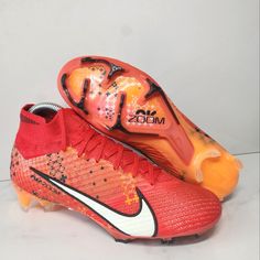 a pair of red and orange soccer cleats on a white surface with black accents