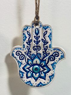 a ceramic hamsa hanging from a rope with blue and white designs on the front