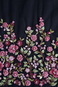 an embroidered fabric with pink flowers and green leaves on black background in close up view