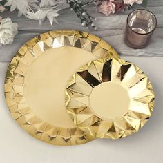 two golden plates sitting on top of a table next to some flowers and vases