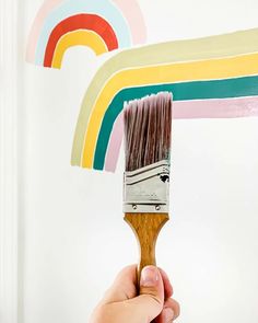 a hand holding a paintbrush with a rainbow painted on the wall in the background