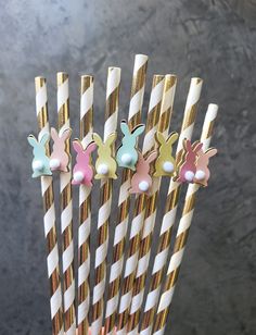 several different colored bunny shaped straws in a cup with gold and white striped straws