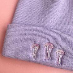 three little jellyfish embroidered on the side of a purple beanie with pink background