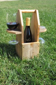 two bottles of wine are sitting in a wooden holder on the grass, with one glass placed between them