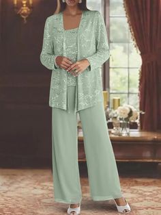 a woman standing in front of a window wearing a green suit and matching pants with white shoes