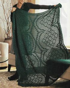 a woman holding up a green crocheted blanket