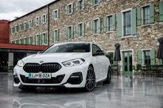 a white bmw car parked in front of a stone building with green shutters on the windows