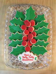 decorated cookies in the shape of a christmas tree on a glass platter with holly leaves