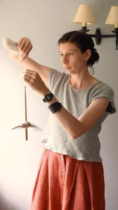 a woman standing in front of a white wall holding something up to her right hand