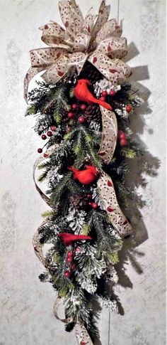 a christmas wreath hanging on the wall with red and white bows, pine cones and berries